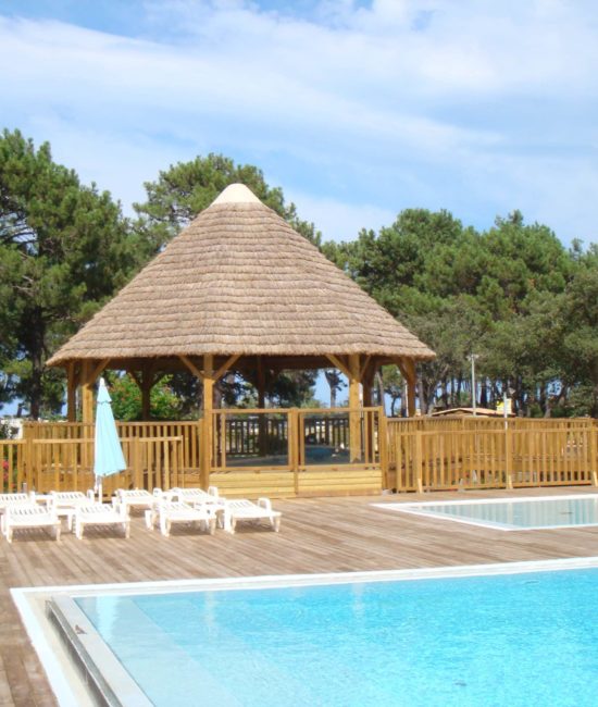 Vue sur une piscine avec à coté une paillote Ekolinea avec une couverture de toit en roseaux. Ekolinea est spécialiste des Parasols exotiques et paillotes.