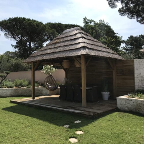 vue sur une paillote Ekolinea dans un jardin privé et entourée d'herbe verte, avec un plancher en bois. Ekolinea est spécialiste des Parasols exotiques et paillotes