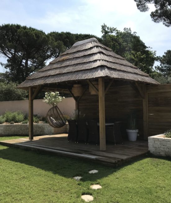 vue sur une paillote Ekolinea dans un jardin privé et entourée d'herbe verte, avec un plancher en bois. Ekolinea est spécialiste des Parasols exotiques et paillotes