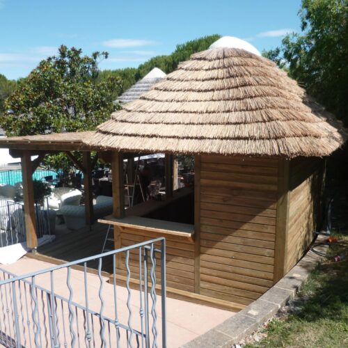 Vue sur une paillote avec un toit traditionnel en roseau de camargue et une pergola. Ekolinea est spécialiste des Parasols exotiques et paillotes
