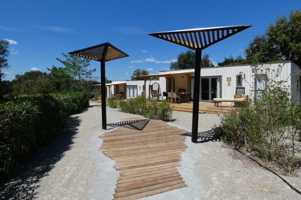 Vue sur un chemin recouvert d'un plancher et de parasols modernes pour faire de l'ombre. Ekolinea est spécialiste dans la conception et construction de Parasols exotiques et de paillotes