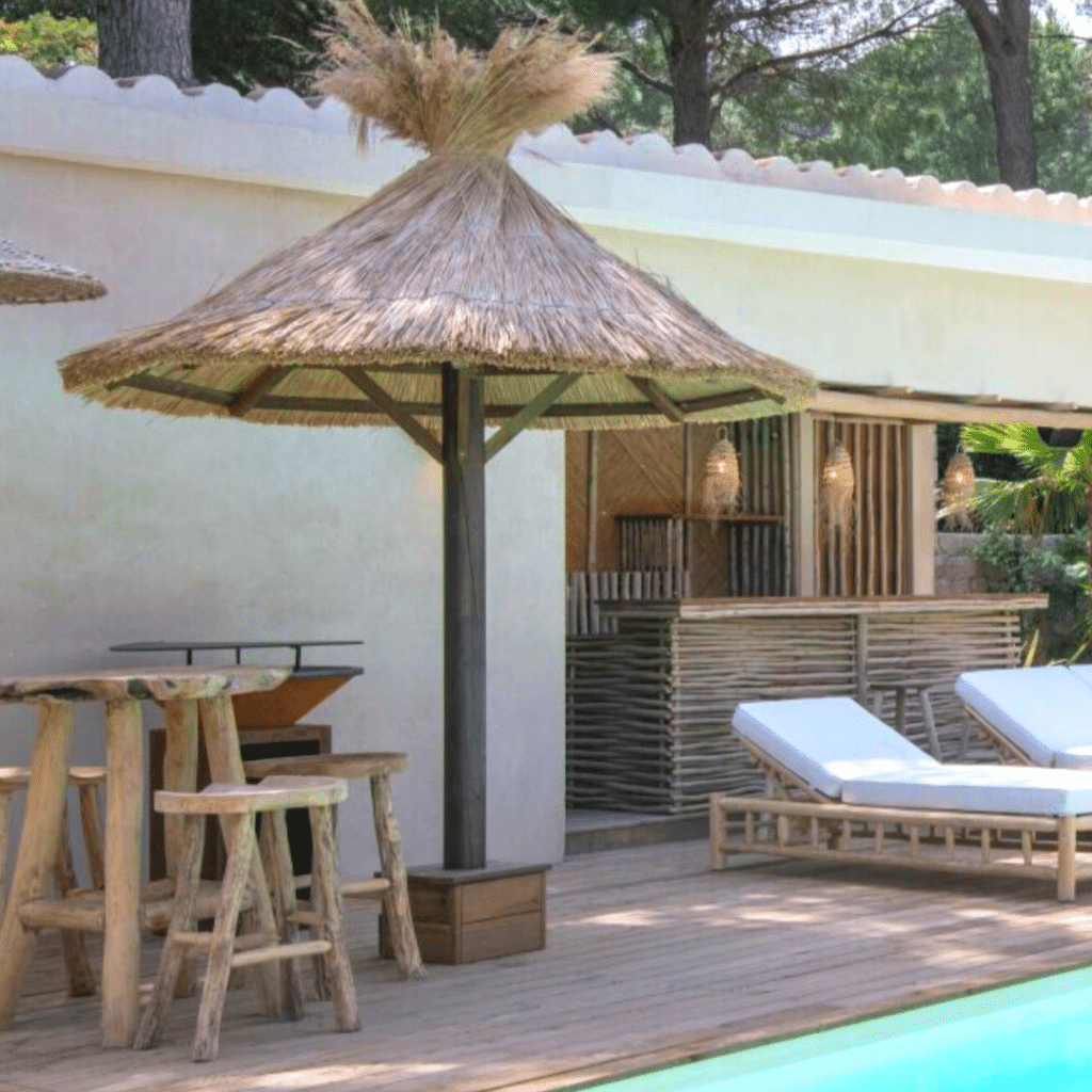 Aménagement extérieur bois et roseau vue sur un parasol ekolinea autour d'une piscine. vue sur un pool house conçu par ekolinea spécialiste en Aménagement extérieur bois et roseau