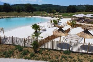 Installation de mobilier (chiliennes en bois) et de parasols camarguais autour de la piscine lagon du Domaine de la Besse en Ariège